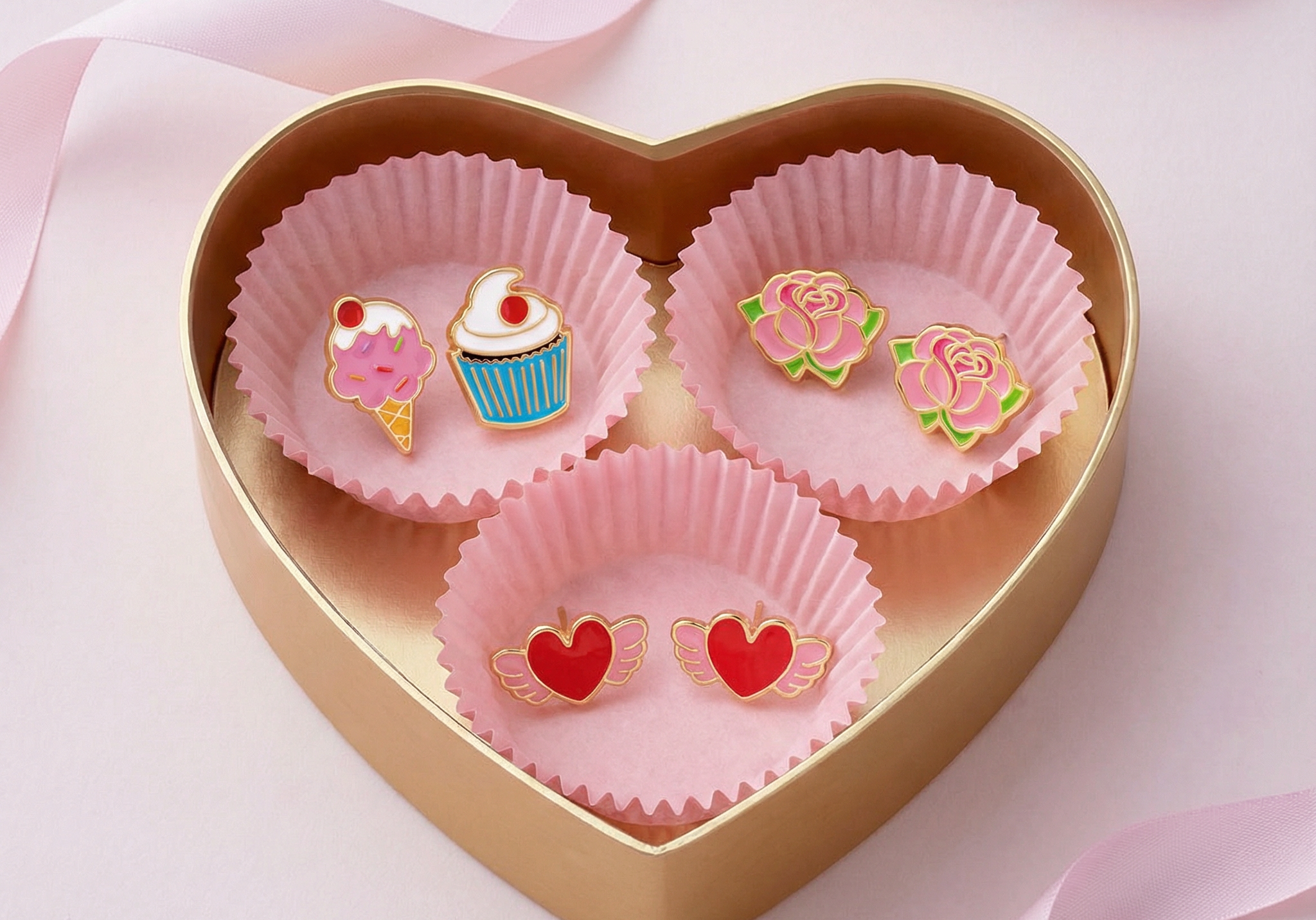 Heart-shaped gift box with dessert, rose, and winged heart stud earrings on pink ribbon background