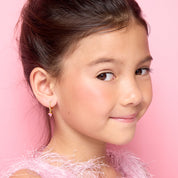 Side profile of a young girl wearing pink CZ heart charm huggie earrings by Girl Nation Canada