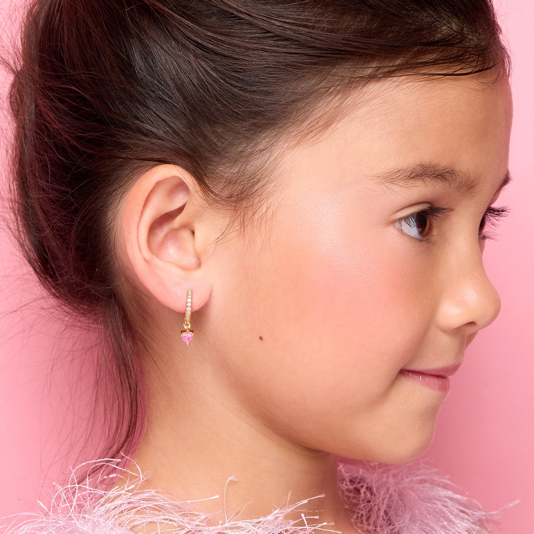 Young girl wearing 18K gold plated pink heart huggie earrings, front view