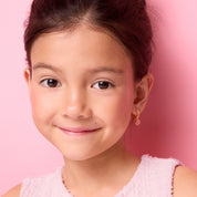 Side profile of a young girl wearing pink CZ flower charm huggie earrings by Girl Nation Canada