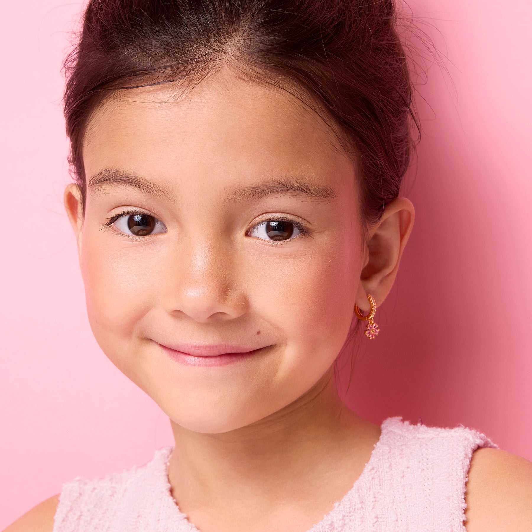 Side profile of a young girl wearing pink CZ flower charm huggie earrings by Girl Nation Canada