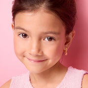 Girl smiling while wearing 18K gold plated pink flower huggie earrings, lifestyle shot