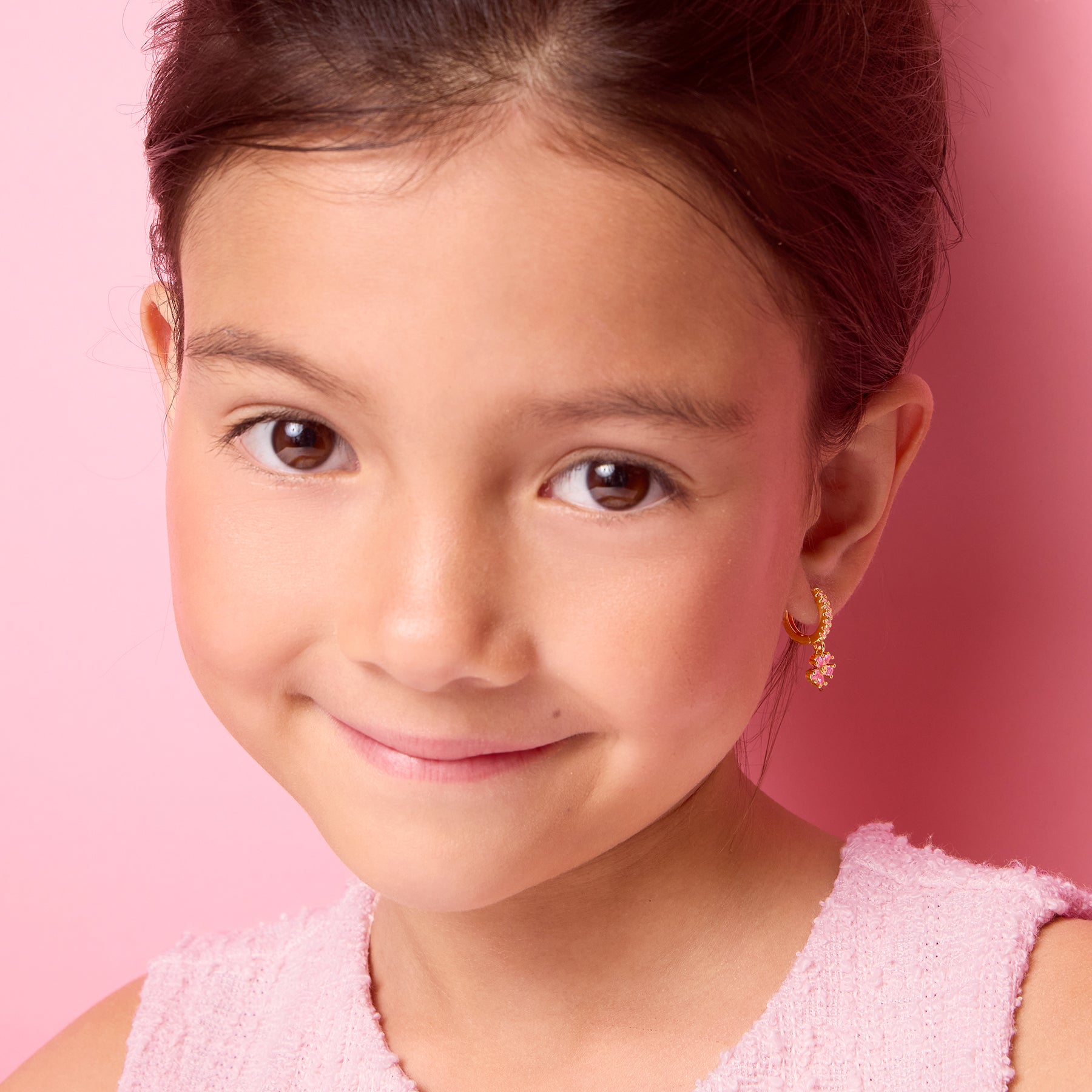Girl smiling while wearing 18K gold plated pink flower huggie earrings, lifestyle shot