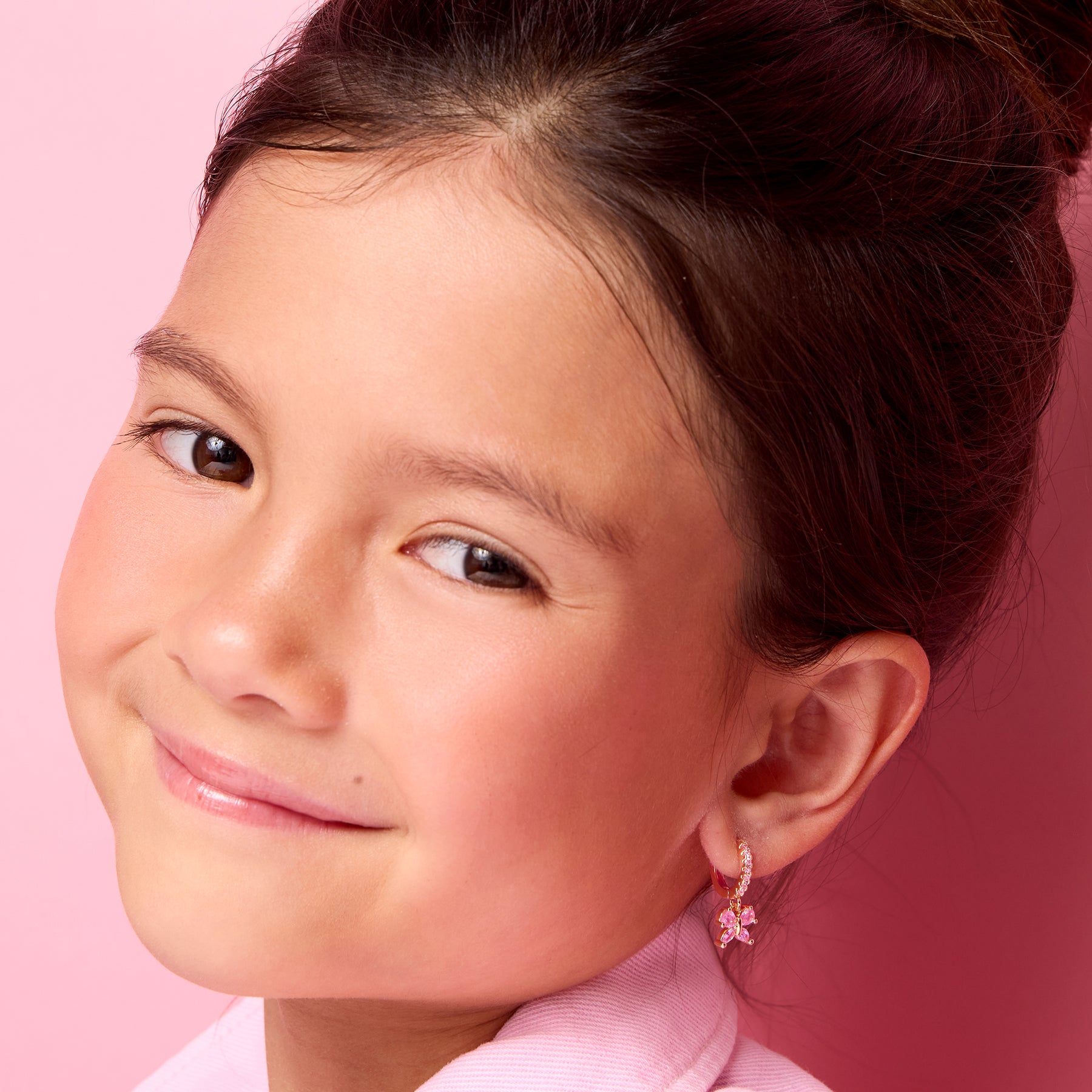 Young girl wearing 18K gold plated pink butterfly huggie earrings by Girl Nation Canada